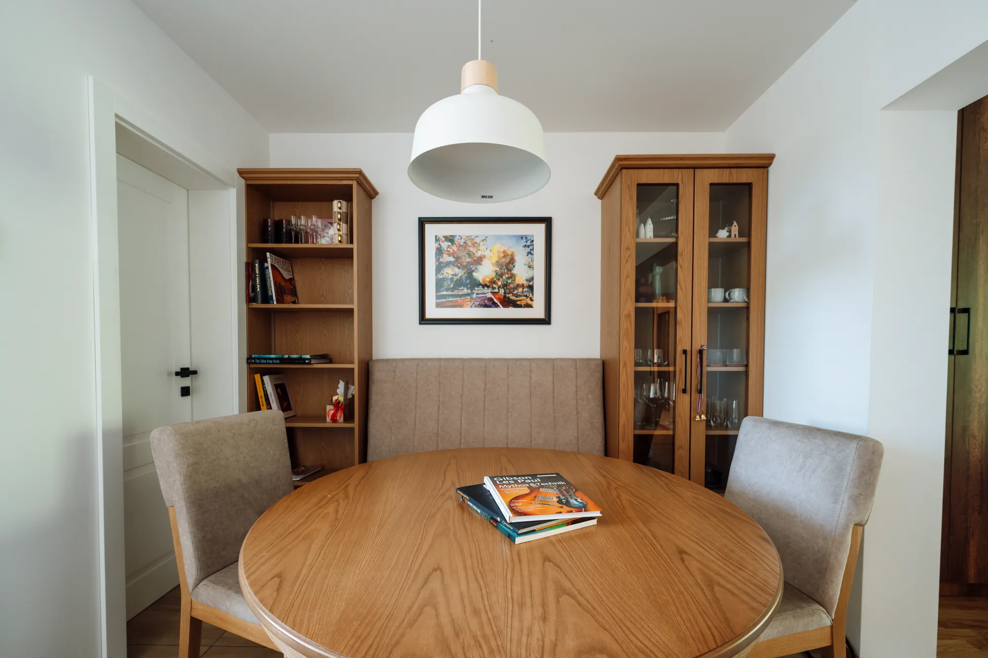 Comedor con mesa redonda de madera bajo una lámpara colgante blanca y dos vitrinas