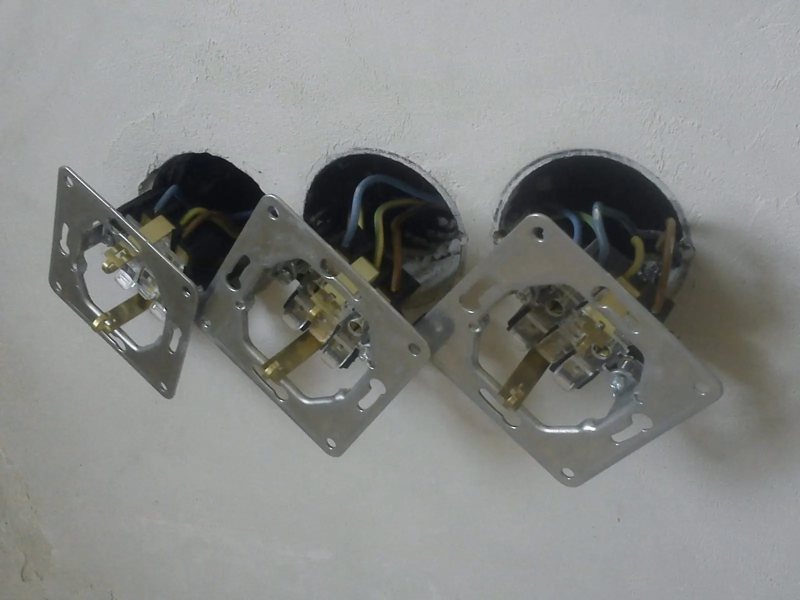 Tres mecanismos de enchufe desmontados colgando de sus cajas empotradas en la pared