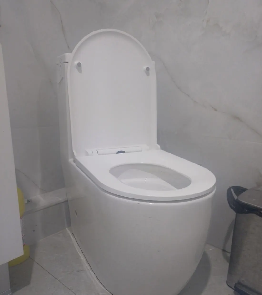 Inodoro blanco moderno con tapa en un baño de paredes de mármol claro