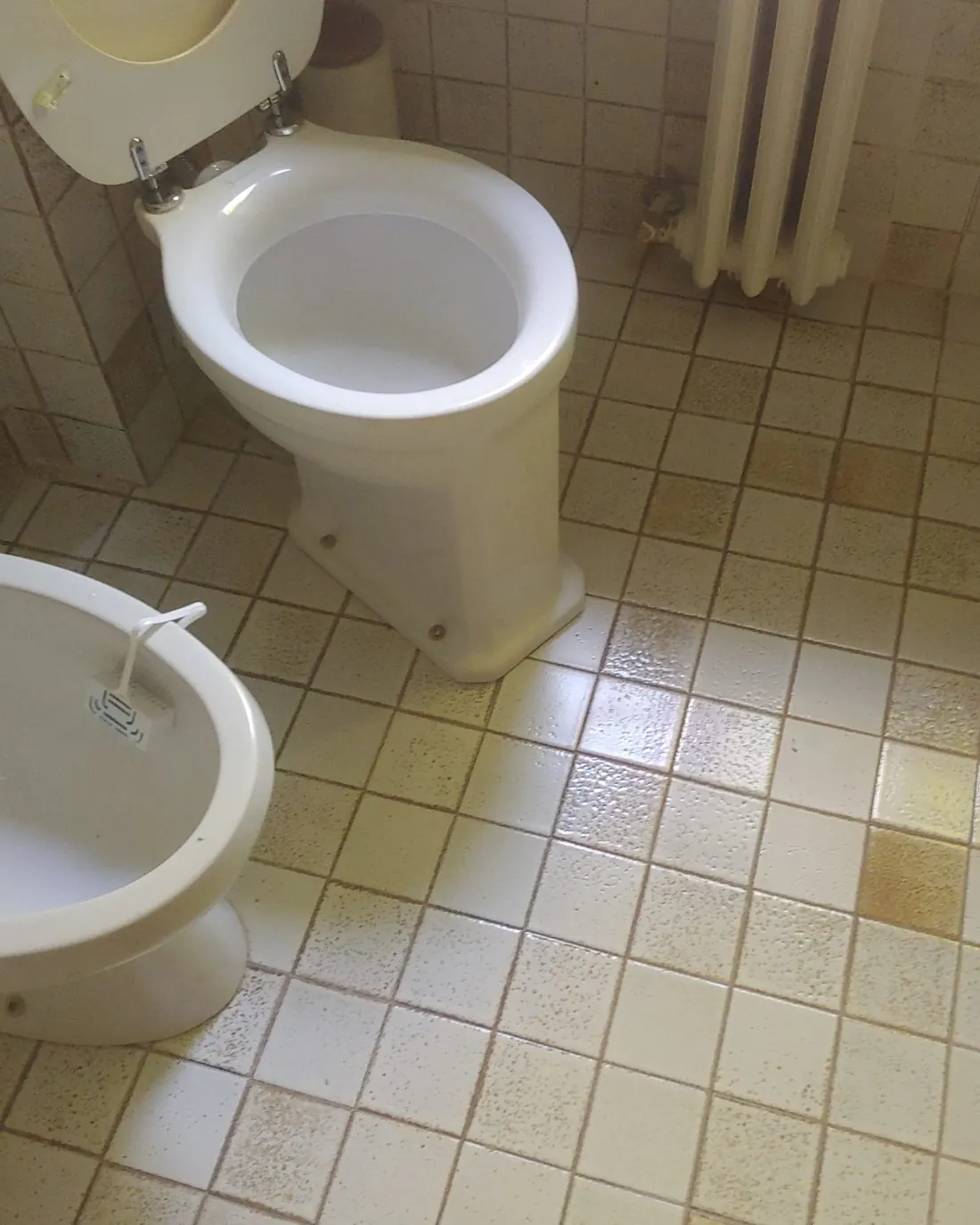 Inodoro y bidé de porcelana blanca en un baño con suelo de baldosa clara