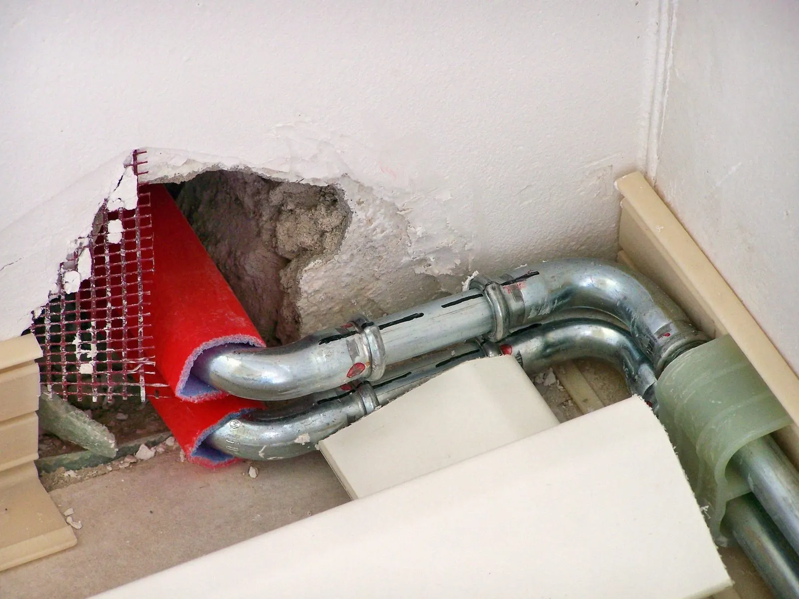 Tuberías metálicas nuevas pasando por un hueco abierto en la esquina de una pared